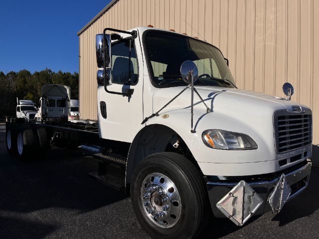 Freightliner M2 cab and chassis truck in white with dual mirrors and chrome bumper, front view showing headlights and front quarter panel.