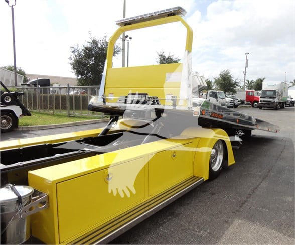 Yellow Peterbilt 337 low-profile tow truck with a tilt bed and raised cab section; stock number J56560; background shows other trucks.