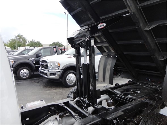 Truck chassis with hydraulic dump bed raised, showing Ram 3500 truck in background. Visible labels include a Venco sticker on the dump mechanism.