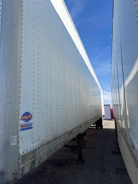 Van trailer side view showing Utility 4000DX badge on the corner with riveted aluminum panels and a blue sky.