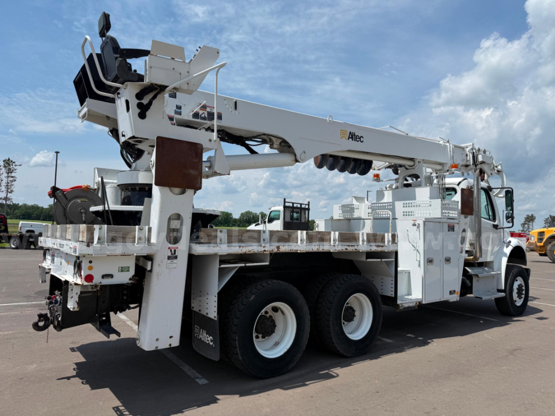A white Freightliner Altec DT65 digger truck with a long boom, mounted stabilizers, and work platform. Side view shows dual rear axles, service compartments, and Altec branding on the boom.