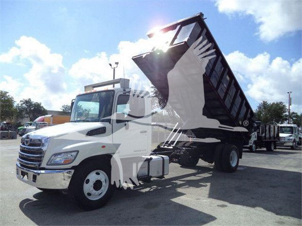 2016 Hino 268A dump truck with raised bed in a dealership lot, white cab, black dump body, stock number T57015, VIN visible.