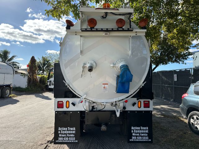 Rear view of a white vacuum truck with circular tank, taillights, and hoses; multiple warning lights on top; company contact info on mud flaps.