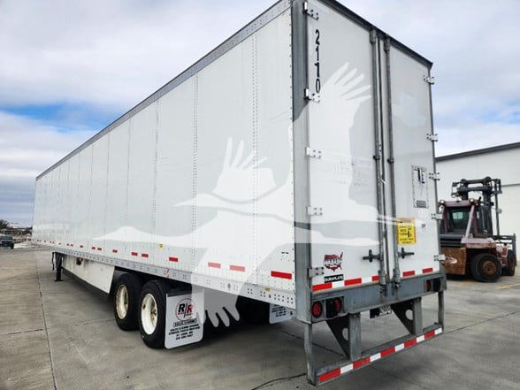 Trailer rear three-quarter view of a 2021 Wabash van trailer with white graphics and a crane bird logo, rear doors closed, stock numbers and VIN notations visible.