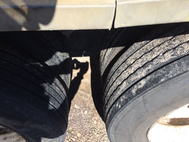Dual truck tires of a Heil trailer with visible tread, wheel wells, and a faint shadow of a camera or person; no legible labels or numbers visible