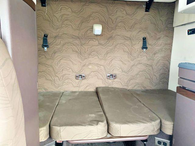 Volvo VNL 670 cab sleeper area with two seat cushions folded flat, beige patterned upholstery, wall hooks, and small white light fixture.