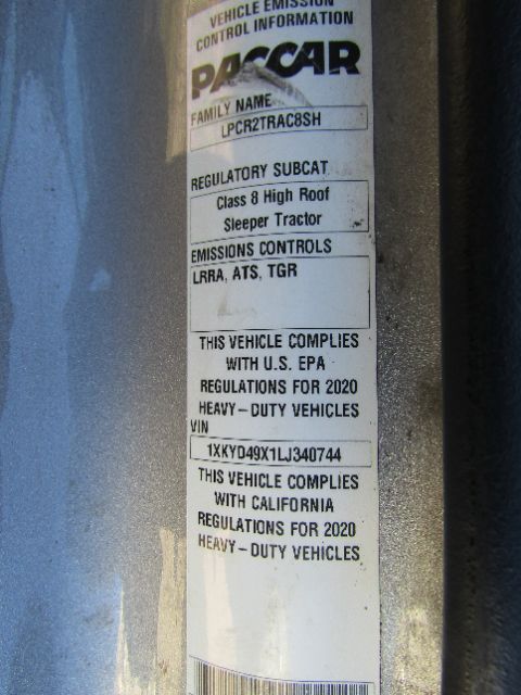 Vehicle identification plate with specifications on a Kenworth truck frame showing Class 8 Tractor, sleeper, tires, and compliance text.