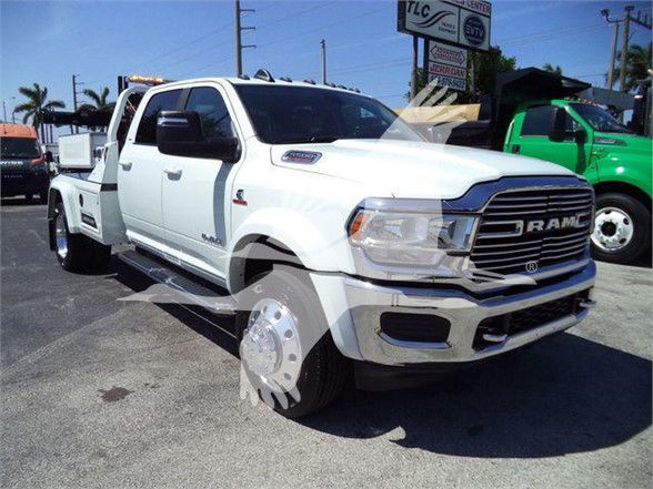 2024 Ram 5500 Laramie tow truck with white cab and dual rear wheels, RAM grille, large chrome bumper, badge on fender, dealership lot in background.