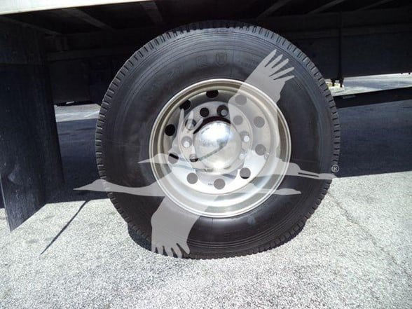 Truck wheel with steel rim and black tire under trailer; watermark overlay partially visible.