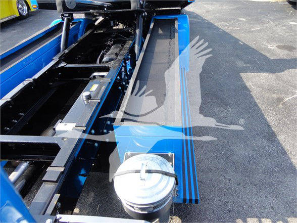 Truck bed frame with blue chassis and hydraulic components. Visible are metal rails, a silver cap on the front, and a fold-out bed structure. Some text and a watermark/logo overlay are present but not legible.