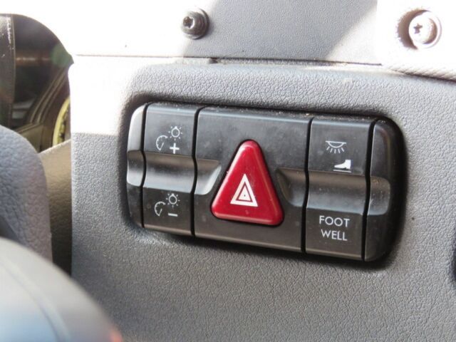 Truck dash panel with central red triangle hazard switch and surrounding buttons including headlight and footwell lights in a Freightliner Cascadia Evolution interior