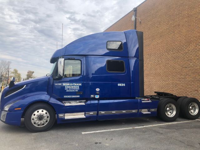 Blue Volvo VNL64T860 sleeper cab side view with World Trade Logistics decals and 9834 stock number.