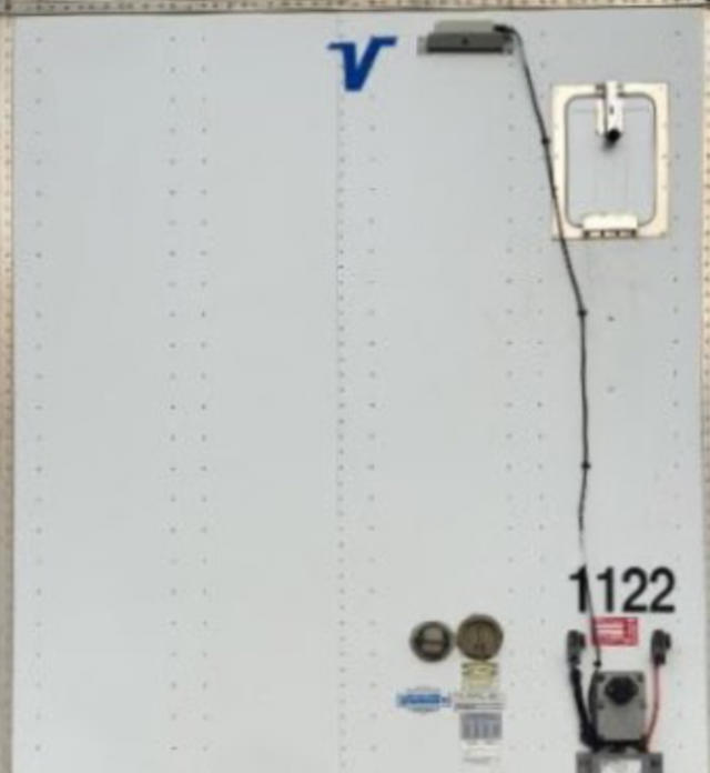 Trailer side door with Vanguard logo 'V' near top, various stickers and serial area including '1122' and circular gauges, and a small access hatch.