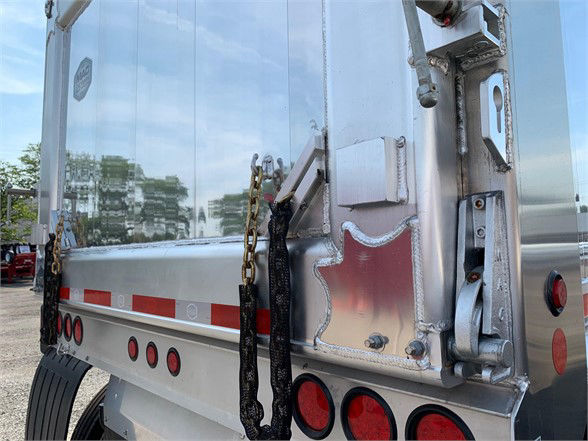 Aluminum dump trailer rear with top hinge door, chain latches, red lights, and reflective tape.
