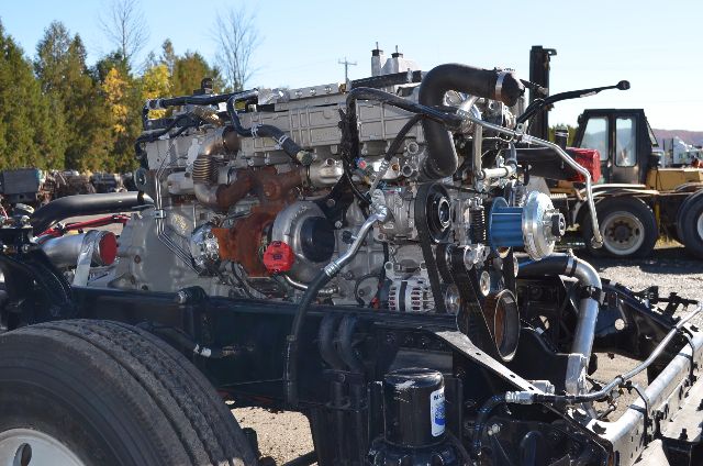 Engine bay showing a Western Star 5700 XE chassis with exposed engine components, belts, hoses, and pulleys.