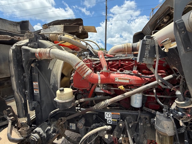 Kenworth W900 engine bay with red engine block, hoses, and exposed components; radiator on left, coolant reservoir, and various wiring harnesses visible.