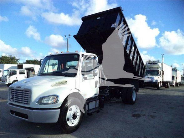 Truck with a raised dump bed in a dealership lot. Front cab shows Freightliner-style grille. No visible text on the truck itself. Background shows other trucks.
