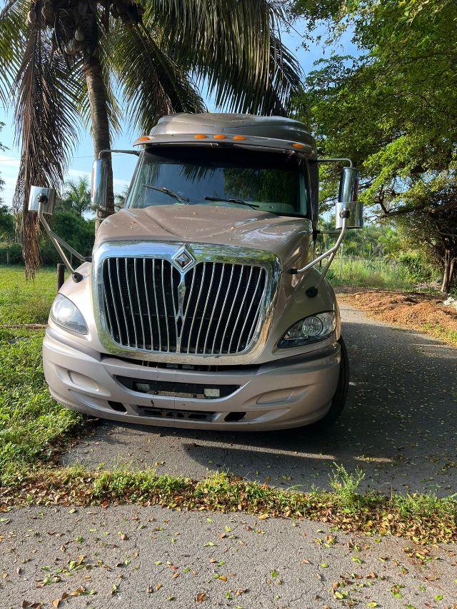 2009 International Prostar front view showing chrome grille, headlights, and sleeper cab; beige/gray truck parked on pavement with palm trees in background.