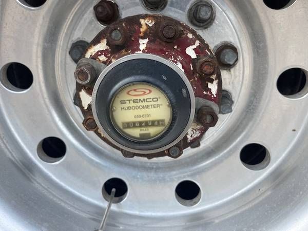 Hubodometer gauge by Stemco installed on wheel hub, showing circular metal hub with bolts and rust around flange.