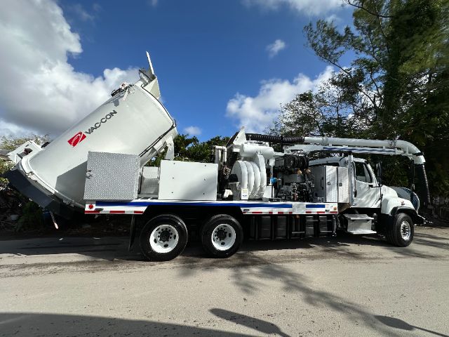 Freightliner 114SD vacuum truck with large Vactor vacuum system, white cab and equipment, side view showing rear-mounted tank and hoses.