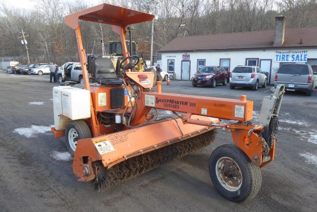 2012 Laymor SM300 inline rotary broom attached to a small orange tractor with canopy, in a parking lot; front brush and rotovibratory sweeper.