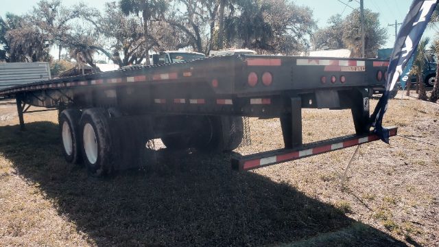 Flatbed trailer showing wheels, frame, and rear ramp with red reflectors and side safety rails.