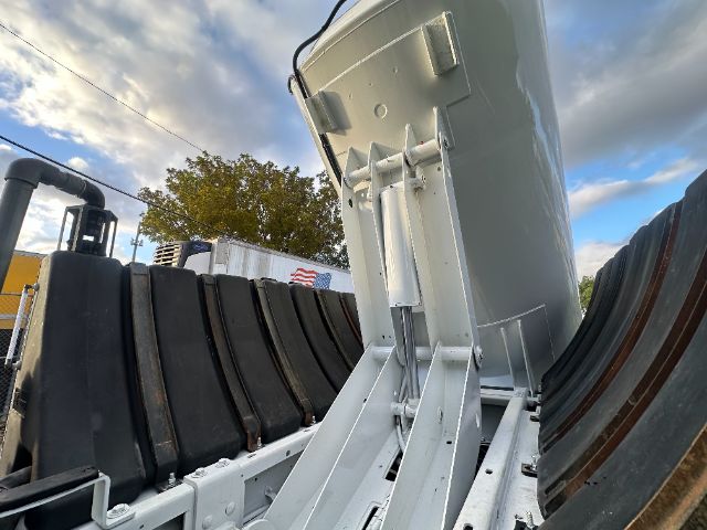 Inline view of a 2016 International 7400 vacuum truck component with tailgate/hoist mechanism and large steel tires in the background.