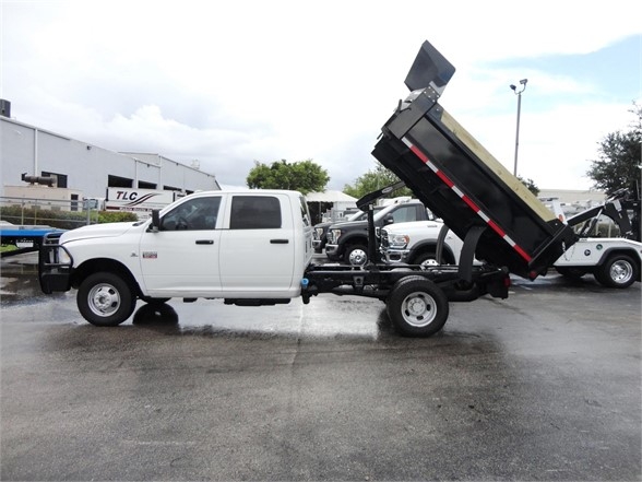 Ram 3500 SLT dump truck with dump bed raised in a dealership lot. Visible text on truck includes RAM badge on front fender and likely model details.