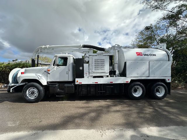 2000 International F-2554 vacuum truck side view showing long vacuum hose reel and Vac-Con branding on silver tanker body.