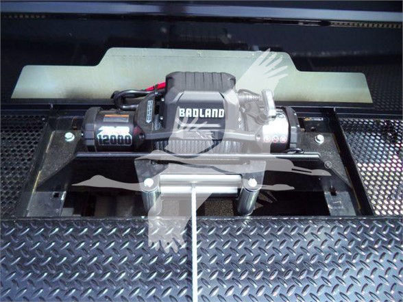 A Badland winch mounted in a Freightliner Business Class M2 106 truck bed, with a diamond plate surface and protective cover.