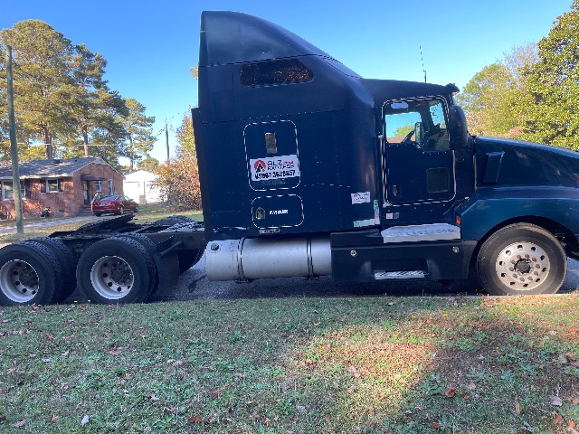 Side view of a dark blue 2007 Kenworth T600 conventional sleeper truck tractor with dual rear wheels and fuel tank, showing sticker labels on the cab.