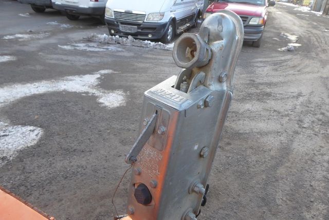 Trucking equipment hitch assembly with a steel bracket, round receiver, and winch-style hook. Visible welding and bolts on a metallic, weathered surface.
