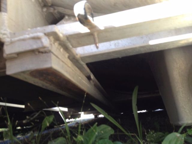 Underbody view of a vacuum tank truck frame showing suspension and metal frame member with some rust spots and grass beneath.