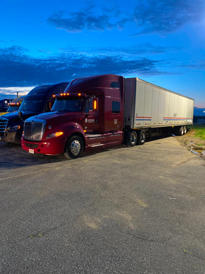 Truck in a parking lot showing a maroon International ProStar tractor with a large white trailer attached.