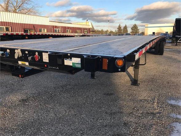 Flatbed trailer showing rear and side frame with manufacturer labels and lighting; visible text includes stock number and model names.