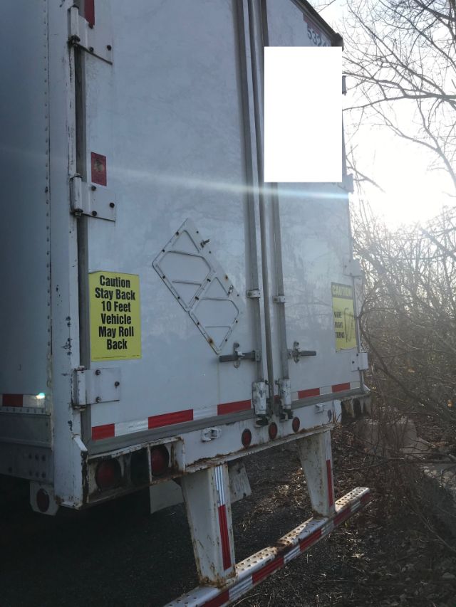 Rear view of a white Pines dry van trailer with warnings stickers, doors closed, and rear underrun protection bar. Yellow caution sticker reads 'Caution Stay Back 10 Feet Vehicle May Roll Back'