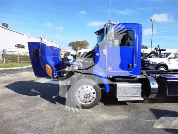 Blue Peterbilt 337 truck cab and chassis with hood open in a dealership lot, showing side profile and front wheel.