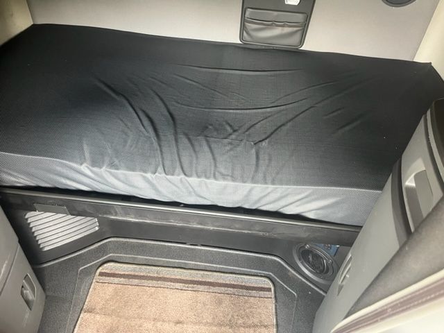 Volvo VNL64T740 truck sleeper interior showing a covered bunk bed with fitted sheet and side cabinet, vehicle dashboard and flooring visible.