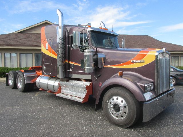Kenworth W900 truck side view showing large chrome exhaust stacks and purple with orange-yellow stripe paint scheme.