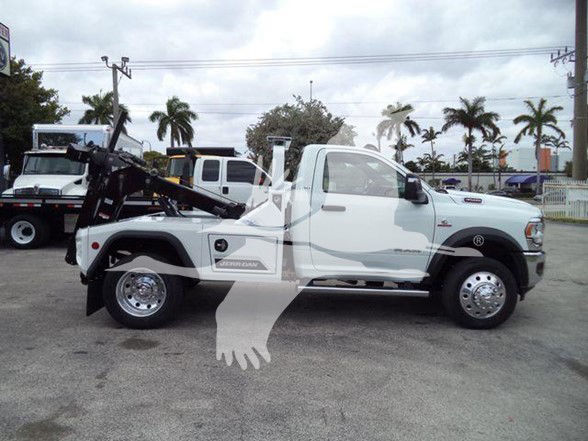 Tow truck with white cab and black boom, Ram 4500 chassis, side view showing wheel wells and hydraulic equipment.