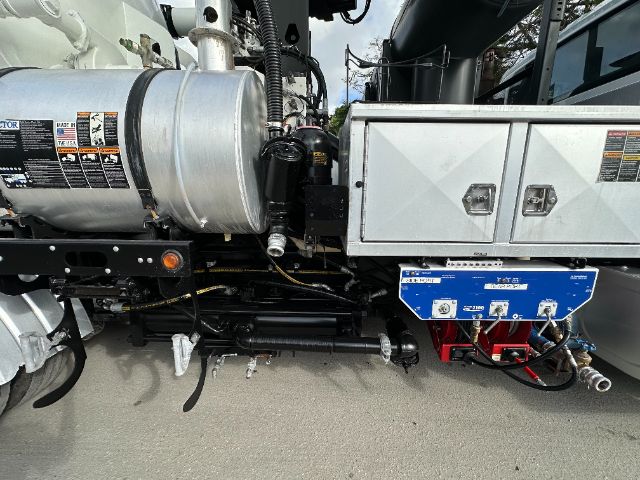 Truck chassis with large engine and a blue electrical module mounted under a silver toolbox; labels and hoses visible.