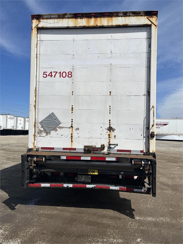 Rear view of a white Wabash dry van trailer with rust along edges and red stock number 547108 on the doors, showing a damaged locking mechanism and a yellow license plate area.