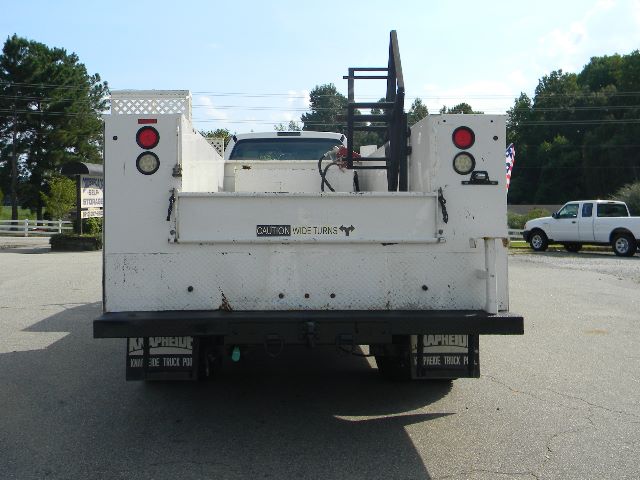 Rear view of a white Ford F-750 service/utility truck bed with safety lights and a platform, showing a 'CAUTION WIDE TURNS' label and some wiring harnesses.