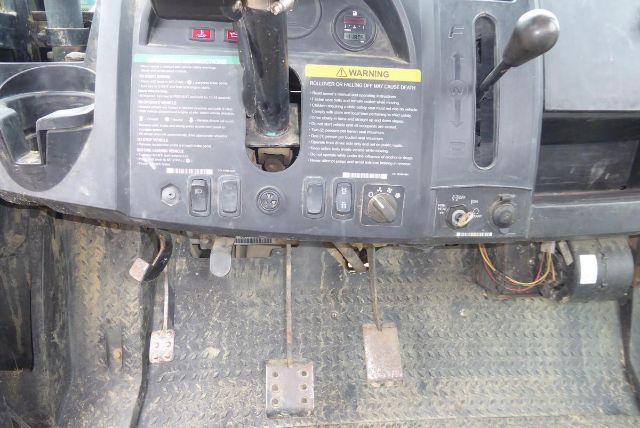 Club Car Carryall 1700 operator area with pedals and control panel. Floor mats, three pedals, switches and warning label on dash. Visible vin area around steering column and wiring harness.