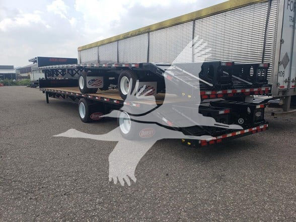 Flatbed trailer with beavertail configuration and dual rear axles, shown from rear-right angle.