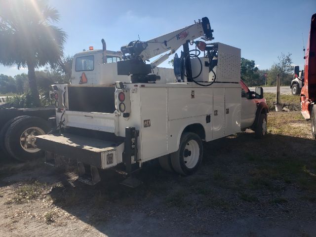 White utility bucket truck with hydraulic crane mounted on bed, rear view shows compartments and tools, Ford cab in background.