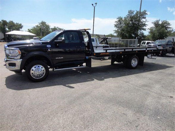 Ram 5500 SLT flatbed tow truck in a dealership lot with a long flatbed and chrome wheels.