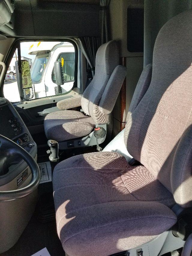 Cab interior of a 2012 Freightliner Cascadia with driver and passenger seats, steering wheel, and side mirror visible.