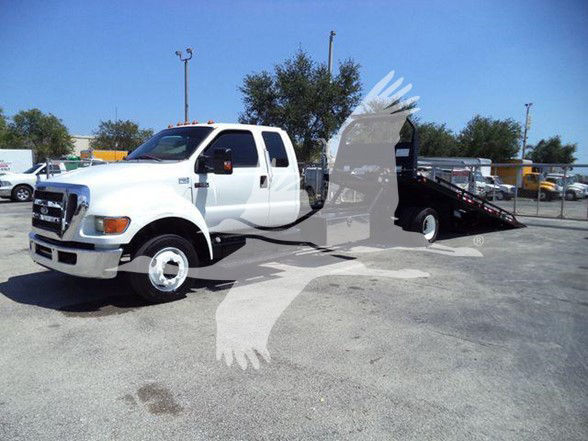 2015 Ford F650 XLT tow truck with a white cab and a black tow bed/dolly in a lot.