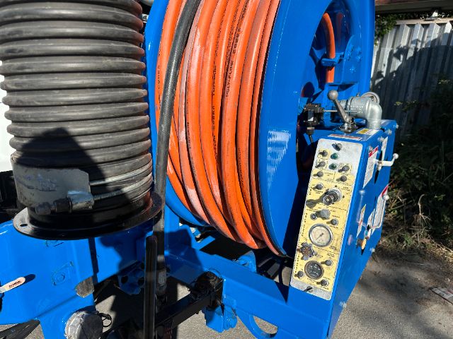 Blue industrial waste vacuum truck reel with orange hose and control panel, coiled cable drum visible.